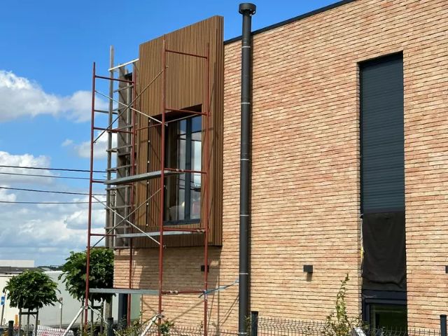 Installation of MexyTech fire-safe WPC cladding on a non-tile exterior wall, featuring wood-tone panels used for facade renovation and insulation upgrades