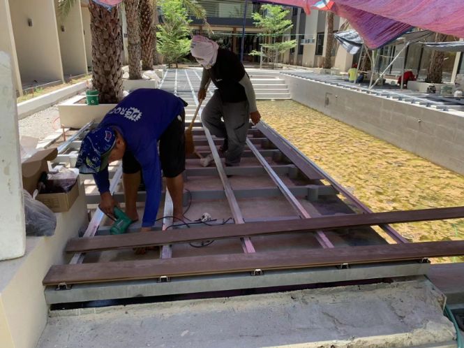 Professional contractors installing WPC decking on an elevated aluminum frame for a poolside project